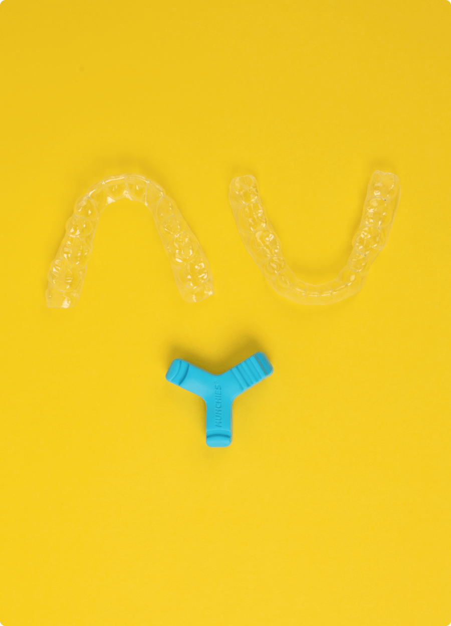 Top down view of Blue Munchies® EPS laying flat next to a pair of clear aligners on a yellow background